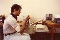 Assistant to Dr. Daniel Graupe demonstrating a computerized arm prothesis, Illinois Institute of Technology, Chicago, Illinois, 1980s